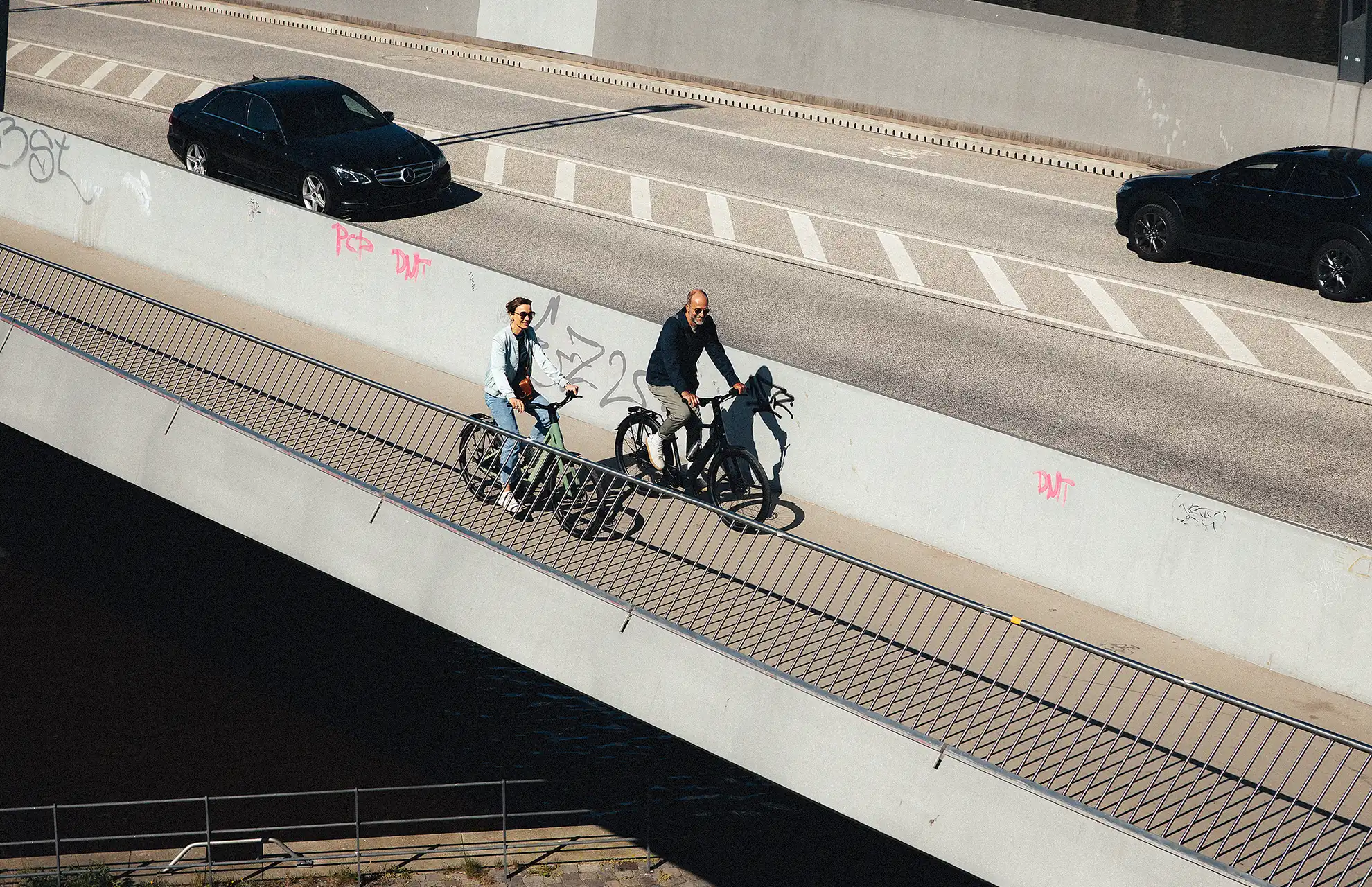 Zwei Radfahrer:innen auf einer Brücke neben einer großen Straße